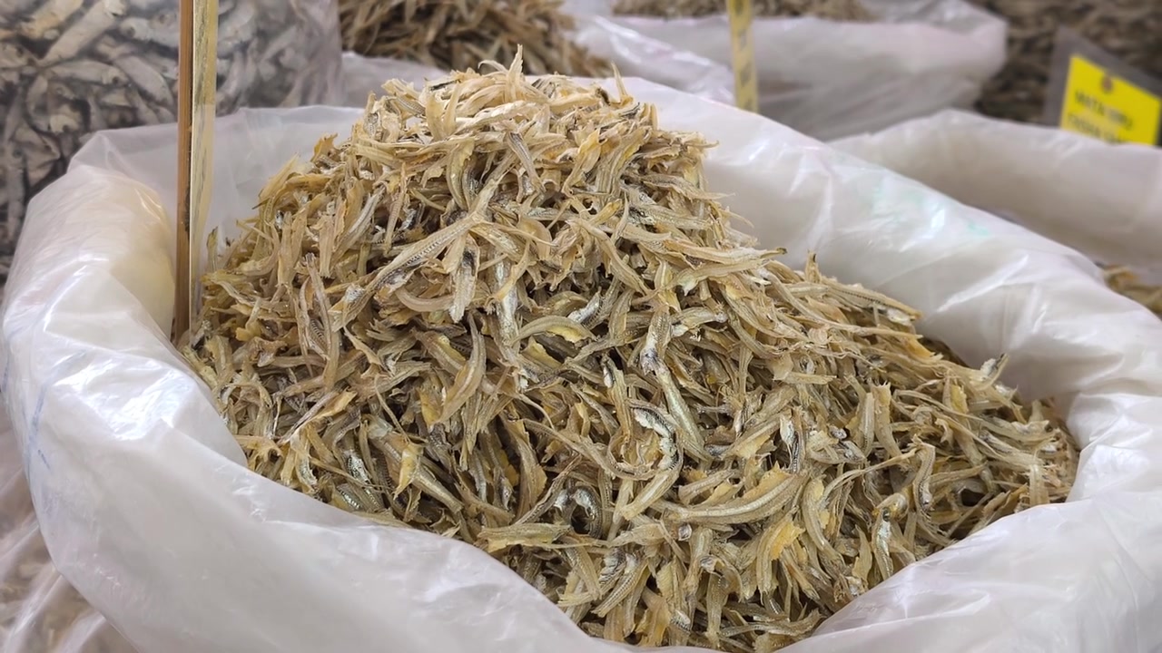 Various categories of dried anchovies are sorted into small sacks for sale. Each grade offers different quality levels and price points for customers to choose from.