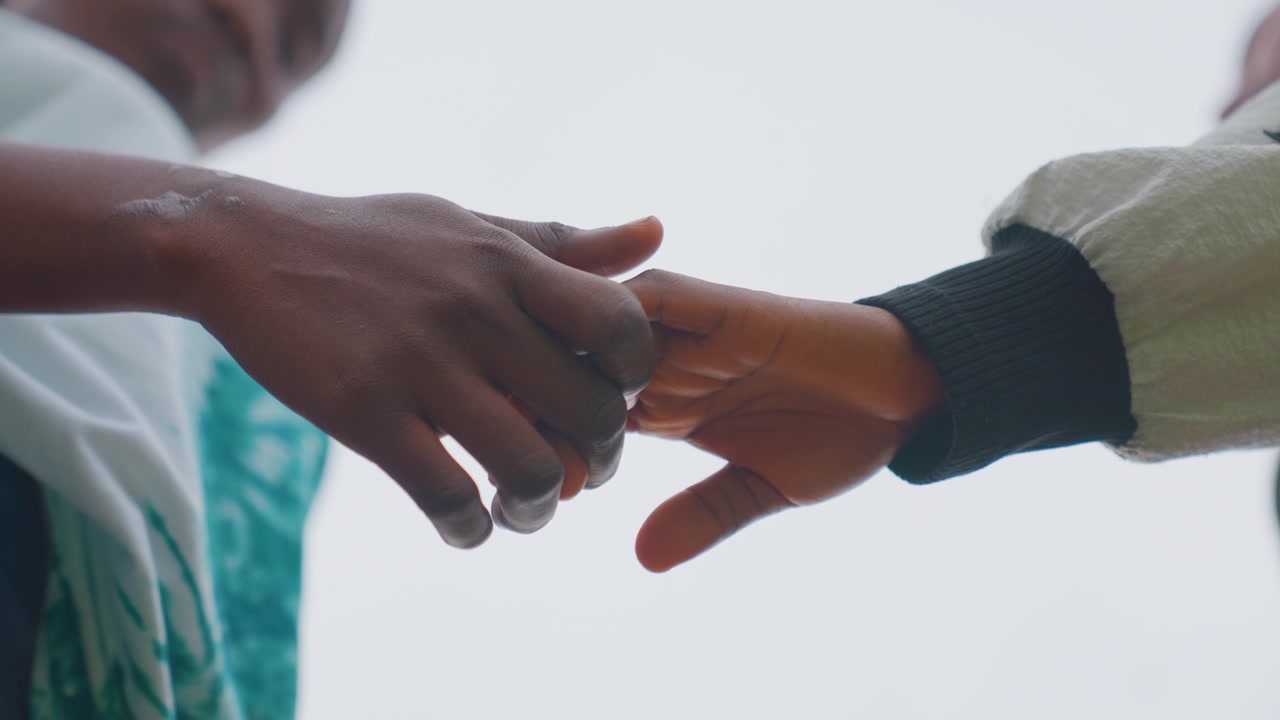 Lowangle black mother and child hands reaching against sky, subtle release, gentle parting gesture, cinematic silhouette, hopeful atmosphere, emotional distance, outdoor minimalism