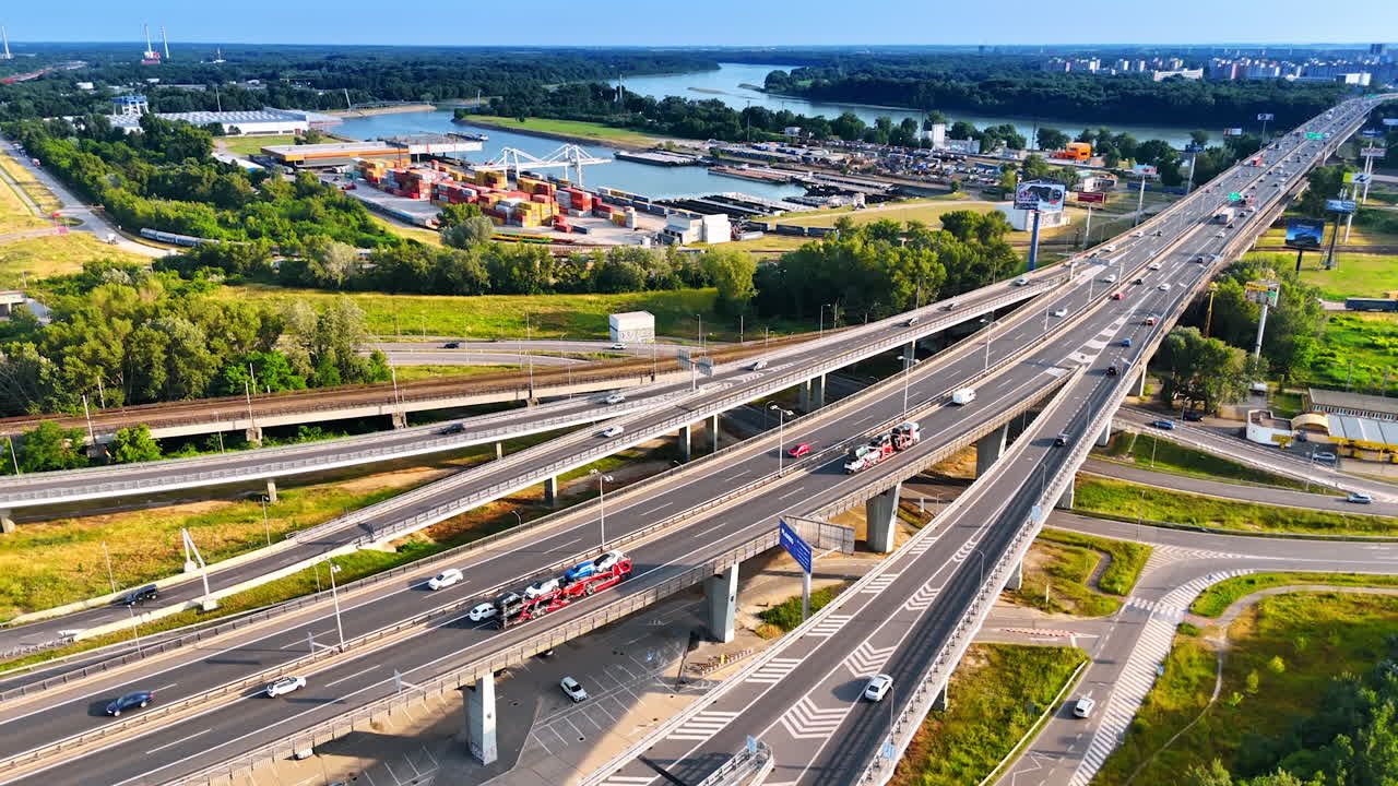 Cars on Euro highway by river. Vehicles travel along a busy highway near a river and industrial area during bright daylight in Europe