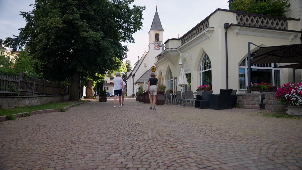 Vista posteriore di turisti che camminano lungo sentieri di strada in mattoni all'ombra di un edificio europeo
