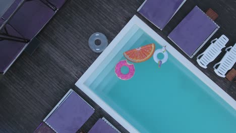 view from the top of the pool with bright colored inflatable circles. a top view of the pool with multicolored inflatable circles and sun chairses standing by the pool. shooting from the drone.