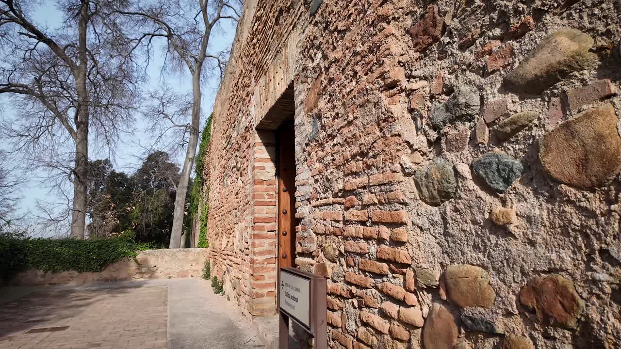 First-person shot of the exterior perimeter wall of the Alhambra monumental complex ending with a panoramic view of the city of Granada, Spain