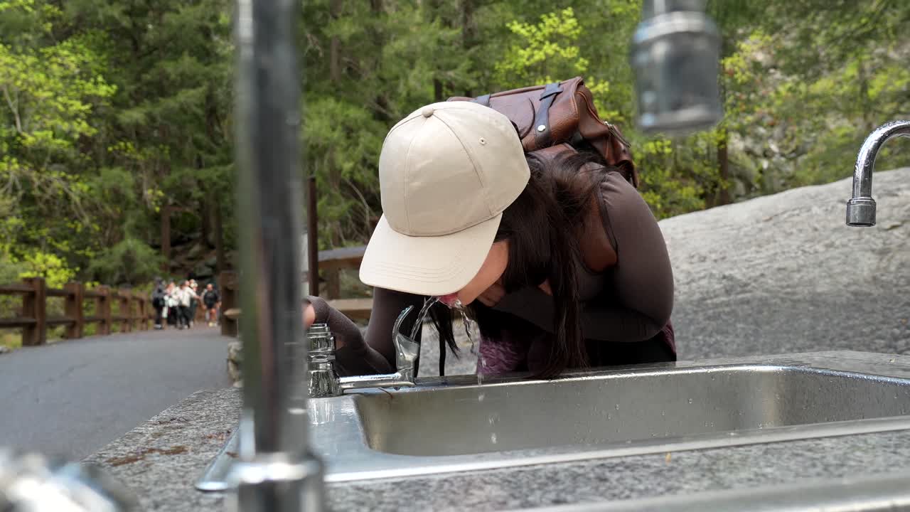Giovane donna che beve acqua rinfrescante da una fontana pubblica all'aperto.