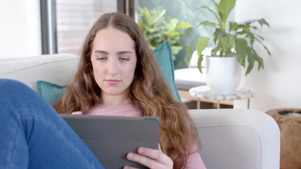 Happy caucasian woman lying on couch and using tablet in slow motion