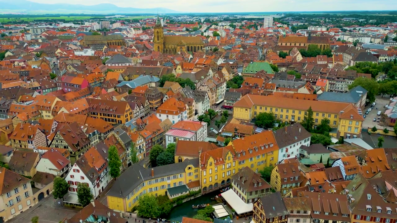 Video aereo con drone 4K delle case a graticcio e degli edifici storici lungo il fiume Lauch che serpeggia attraverso la zona della Piccola Venezia di Colmar, Francia.