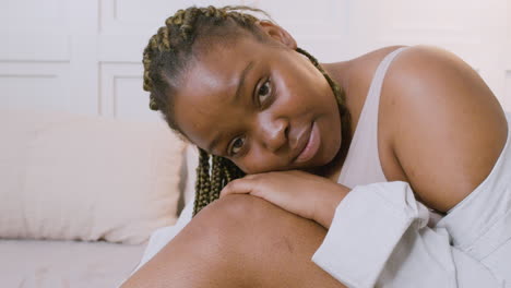 close up view of woman sitting on the bed and posing her head over her knees looking at camera