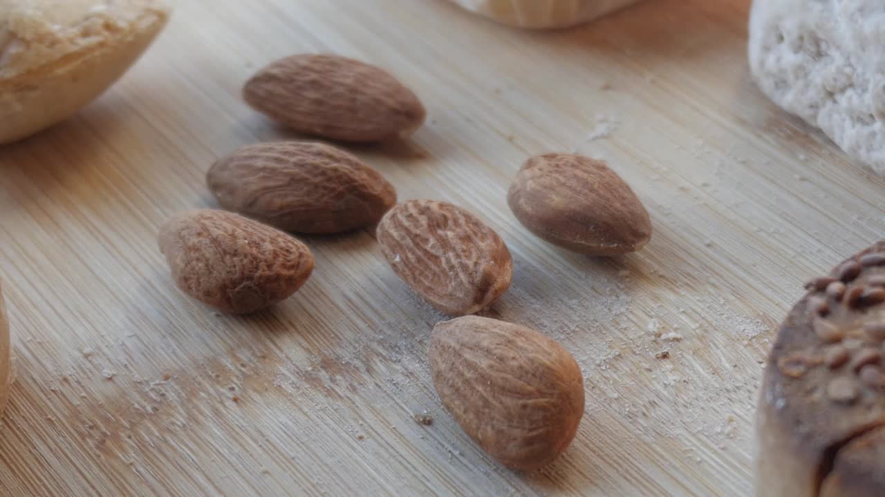 Un primo piano di mandorle sparse su una superficie di legno, circondate da rustici dolci natalizi spagnoli: polvoron, mantecado, rosco de vino.