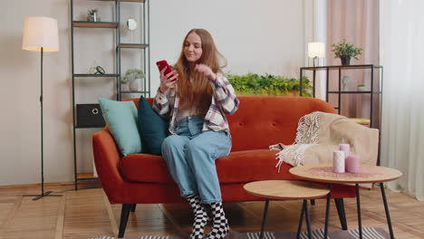 cheerful young woman sitting on sofa, using mobile phone share messages on social media application