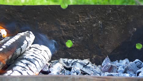 burning wood an coals in rusty portable outdoor bbq grill in sunny day, close up shot