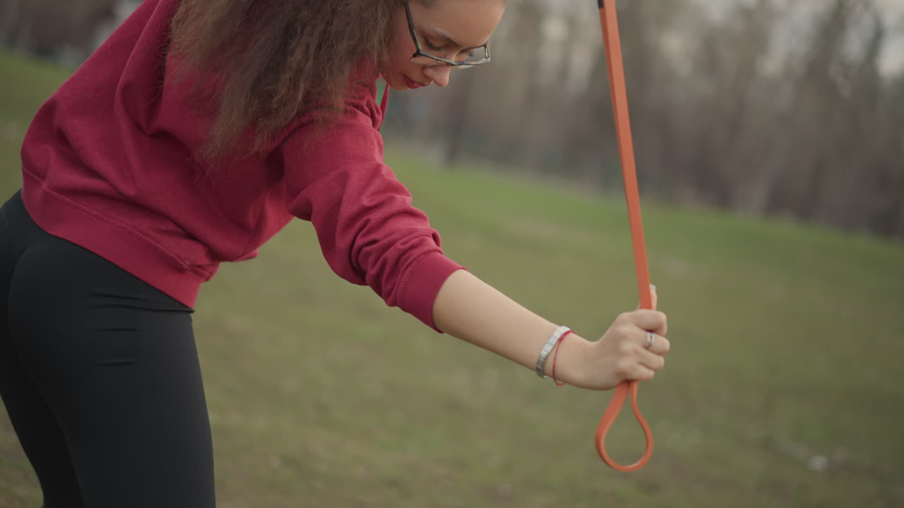 White Woman Rotating Band For Rotational Strength In Park, Athlete Performing Targeted Core And Oblique Conditioning With Controlled Swing, Casual Training Gear And Focused Expression