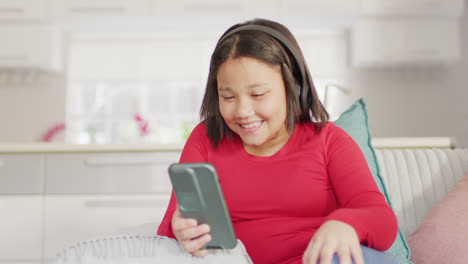 Video-of-happy-asian-girl-resting-on-sofa-with-smartphone