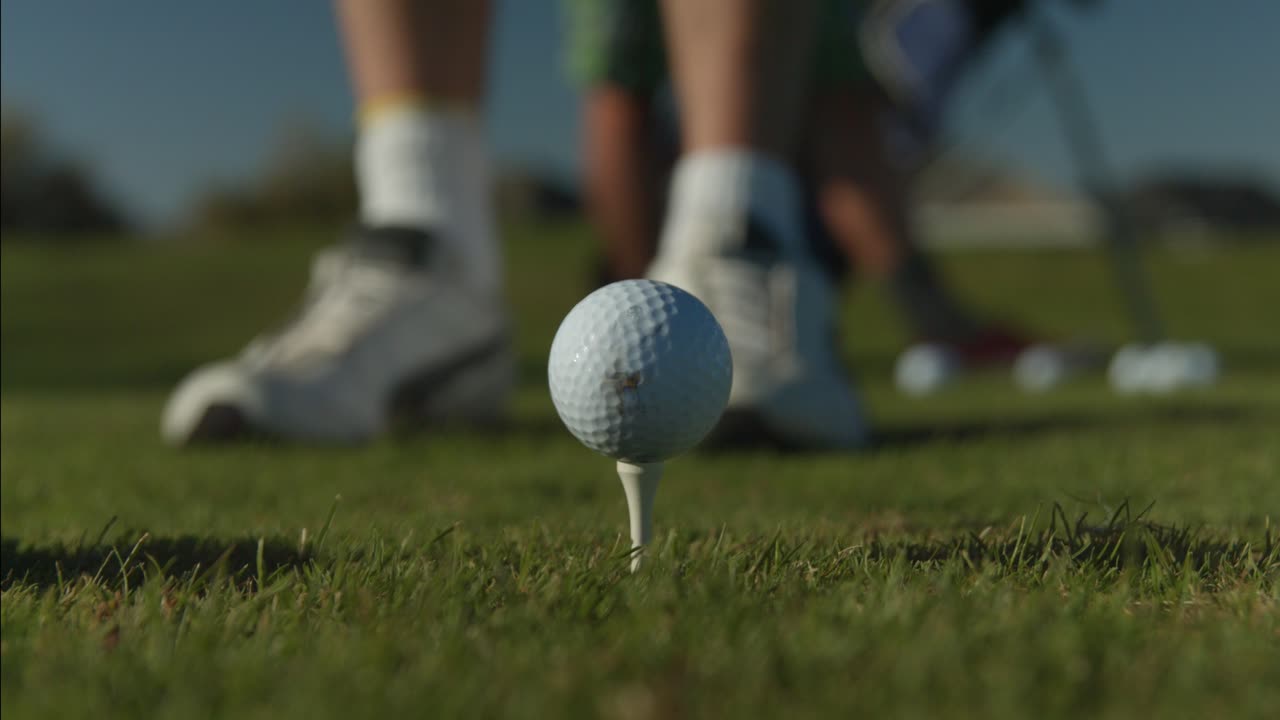 티 센터 프레임에 있는 골프공의 클로즈업과 그의 클럽으로 샷을 정렬하는 골퍼