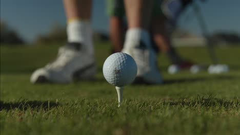 un primer plano de una pelota de golf en el marco central de un tee y el golfista alineando su golpe con su palo