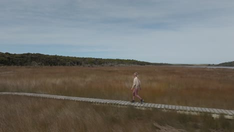 Female-traveler-visiting-Tautuku-Estuary-walkway-in-New-Zealand,-aerial