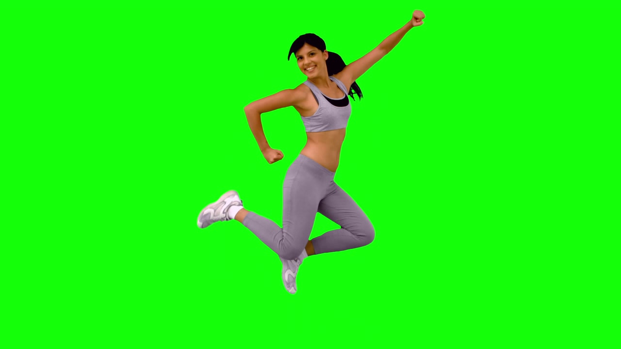 Donna atletica che salta e posa su schermo verde