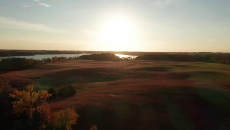 Ethereal-aerial-shot-approaching-the-setting-sun,-over-rolling-hills-with-trees-and-grass