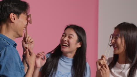 group of young friends in front of pink studio background having fun posing for photo booth style portraits with props 2