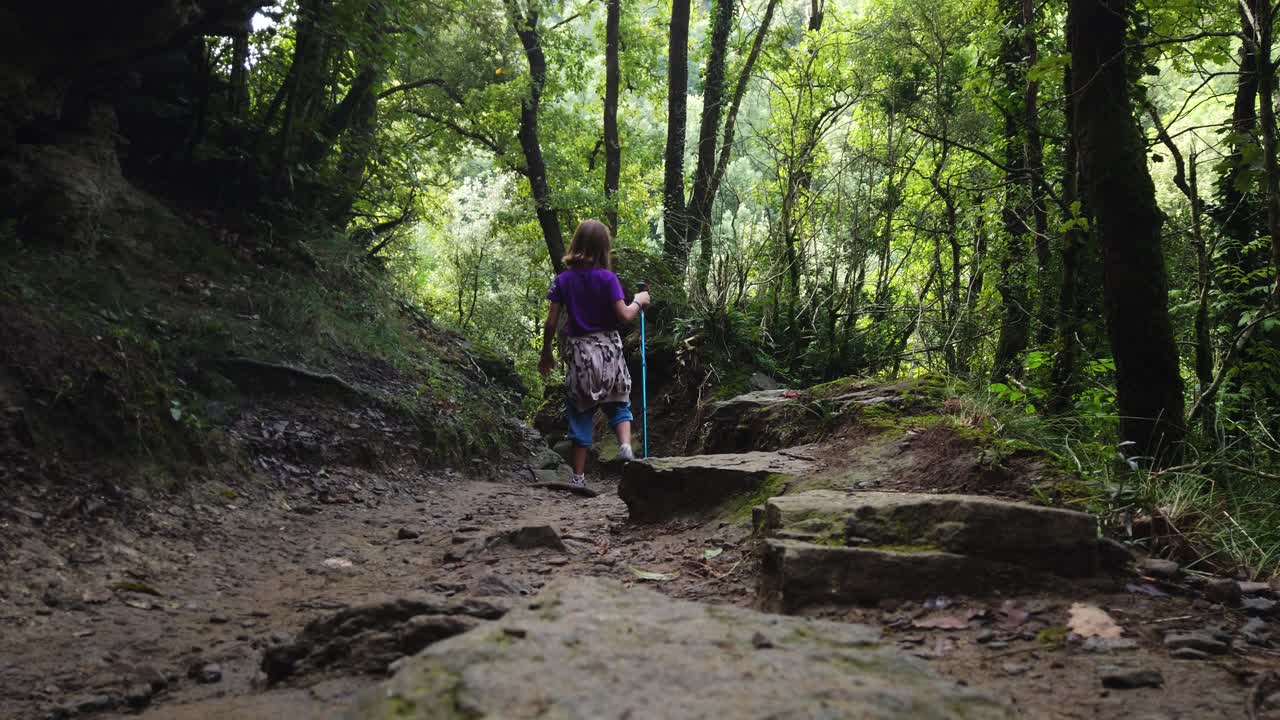 Menina fazendo trilha por uma floresta verdejante em uma trilha rochosa com um bastão de caminhada. Criança saudável aproveitando uma aventura ao ar livre e explorando a bela paisagem natural da Catalunha, Espanha
