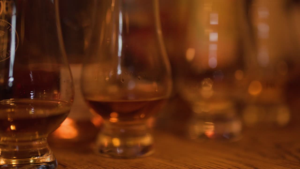 Una mano si allunga verso un bicchiere Glencairn pieno di whisky ambrato nella calda illuminazione di un pub