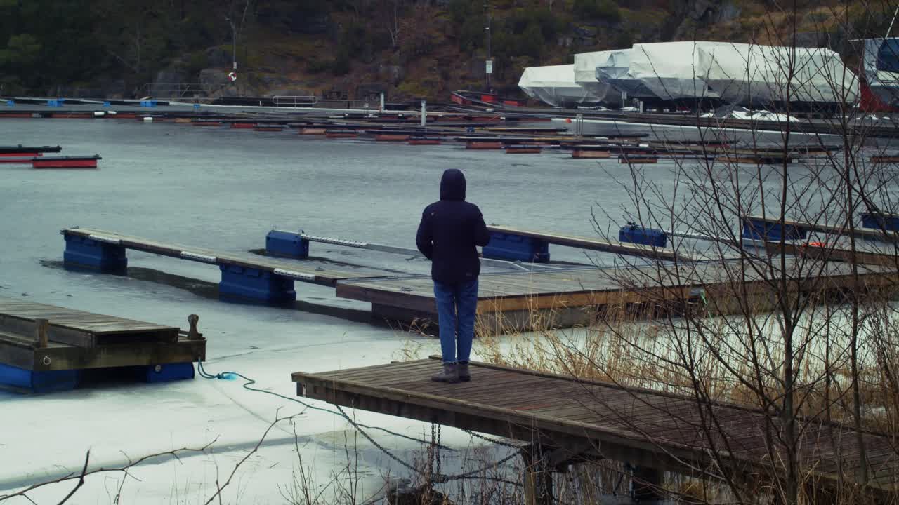 Man met capuchon staand op een pier in Oslo, Noorwegen. Statisch.