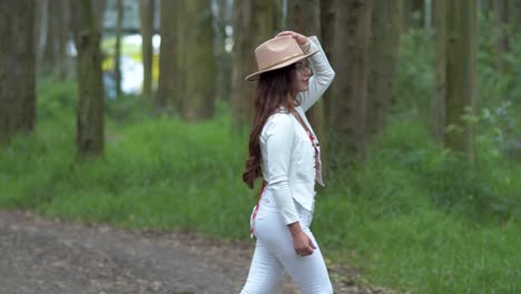 beautiful woman walks through nature and puts a hat on her head