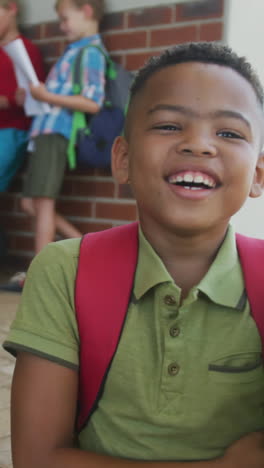 video of happy african american boy holding books in front of school