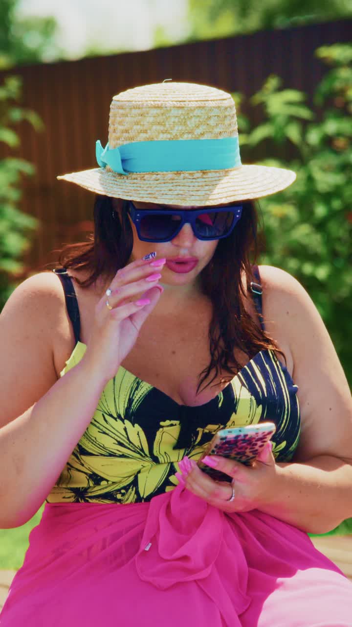 A vibrant summer scene capturing a woman in a stylish hat and sunglasses, engrossed in her smartphone while enjoying the sunny outdoors in a cheerful colorful outfit