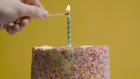 studio shot of revolving birthday cake covered with decorations and single candle being lit 1