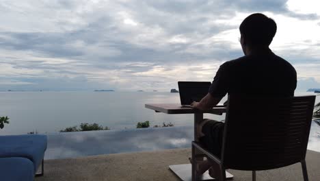 asian man working on the laptop by the pool - back view 2