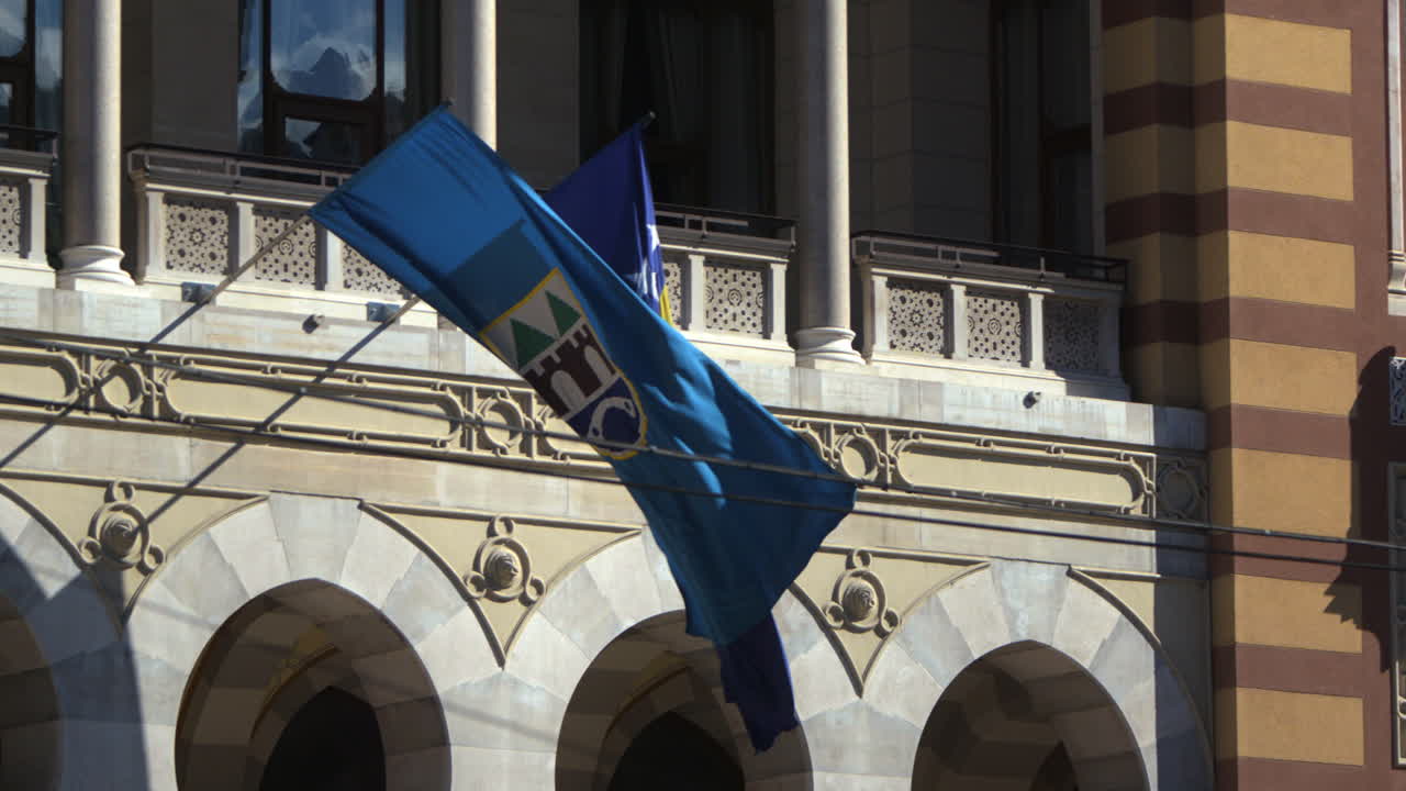 A Bosnia and Herzegovina flag blows in slow motion at Sarajevo capital building. Cinematic view as flag is blowing in the wind.