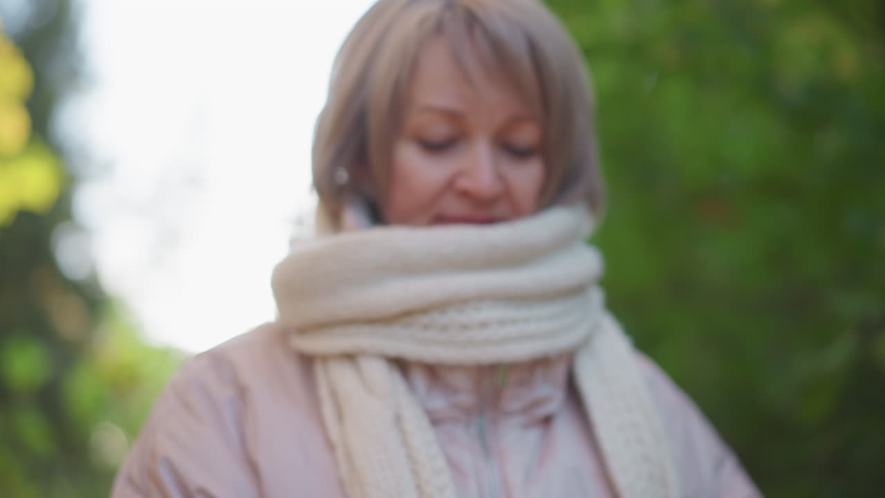 close up of woman flipping through book page with bright red autumn leaf in hand while walking through forest trail, cozy scarf and jacket, soft bokeh foliage background