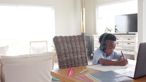 niño afroamericano feliz con auriculares usando computadora portátil para clase en línea en casa, cámara lenta