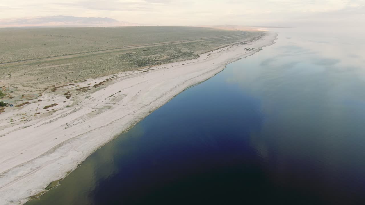 visión aérea del mar de sal, el lago salado y las montañas, las llanuras saladas que reflejan el sol, las nubes y el cielo azul, la simetría que refleja el paisaje aéreo movimiento panorámico, tiempo soleado, nubes bonitas