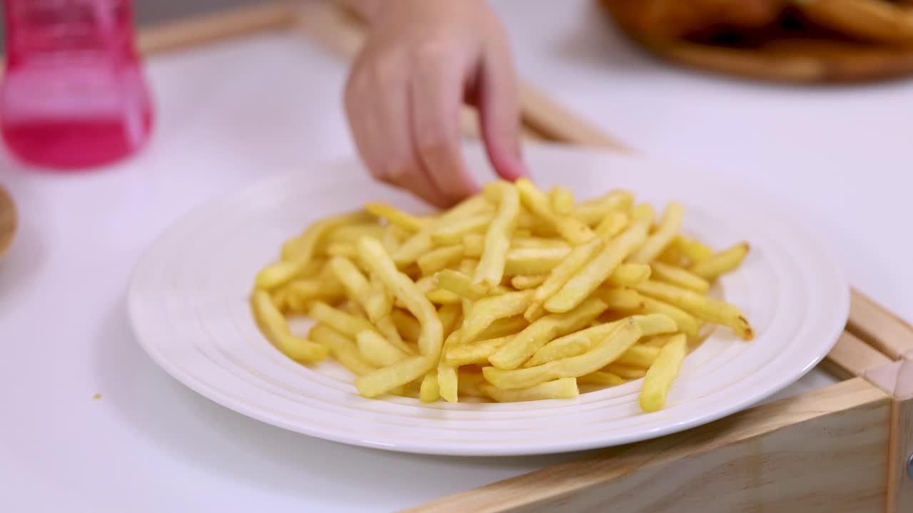 Close-up of child hand grabbing french fries from white plate under bright soft lighting
