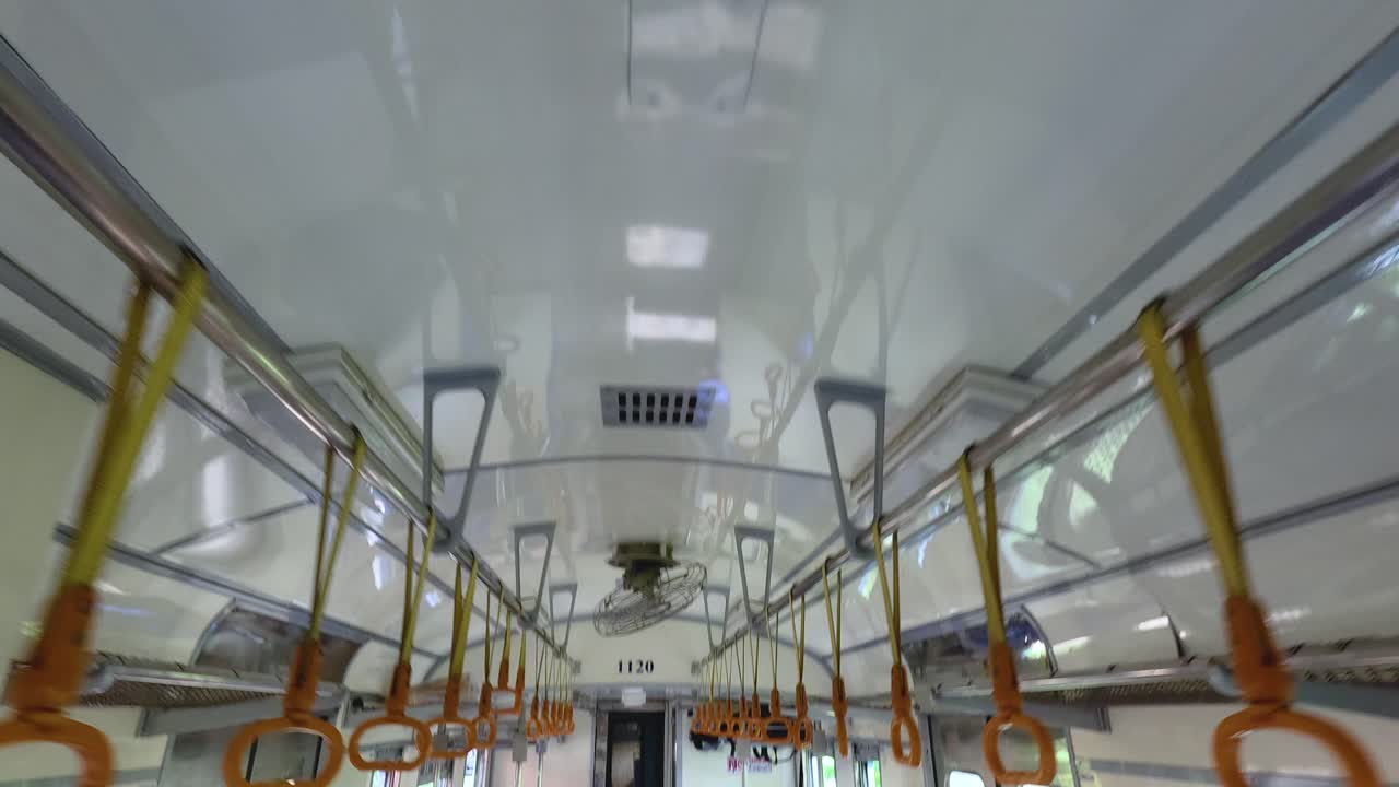 Interior of a train in Kanchanaburi, Thailand, showing fans, handrails, and luggage. Bright lighting and steady camera capture the journey