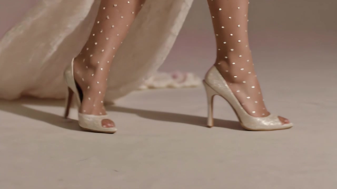 Spostando il peso, una modella avanza in studio, mostrando calze, tacchi peep-toe e lo strascico dell'abito.
