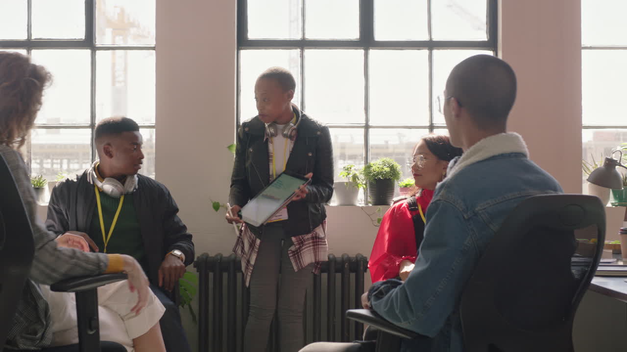 젊은 사업가 들 이 아프리카계 미국인 을 만나는 팀 리더 여성 은 태블릿 컴퓨터 를 사용 하여 창의적 인 프로젝트 아이디어 를 화면 에서 보여 주는 전략 을 공유 하는 동료 들 이 사무실 브리핑 에서 협력 하는 것