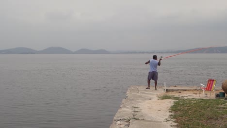 local man throws fishing rod with bait in the water. - wide shot