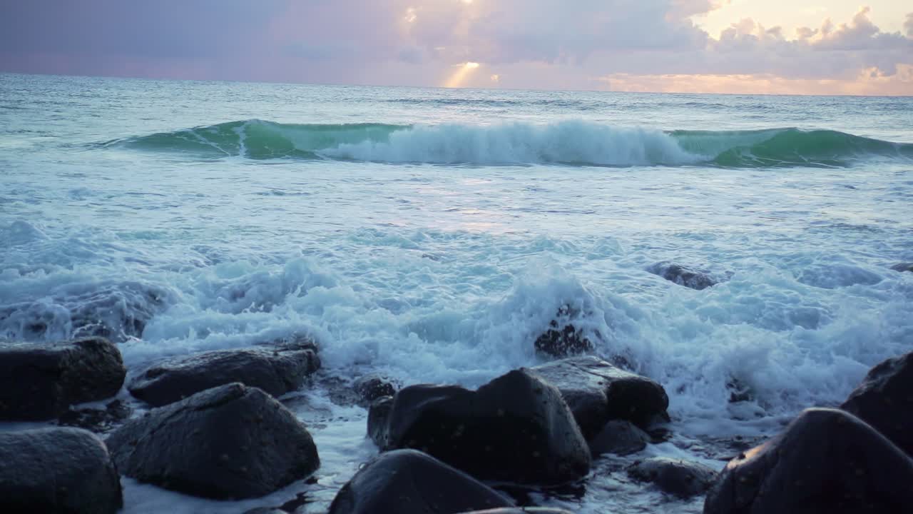 A dramatic cloudy sunrise at Burleigh Heads with waves crashing over exposed rocks. The stunning scene captures the power of nature and the beauty of the Gold Coast coastline.
