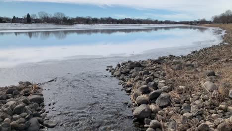 Stream-of-water-draining-from-frozen-lake-into-a-stream,-wide-shot,-no-persons