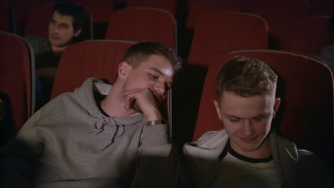 two guys looking smartphone in cinema. friends having fun with phone at theatre