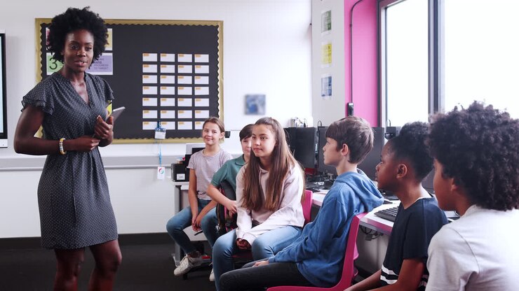 Line Of High School Pupils Raising Hands To Answer Question Asked By Teacher In ICT Class