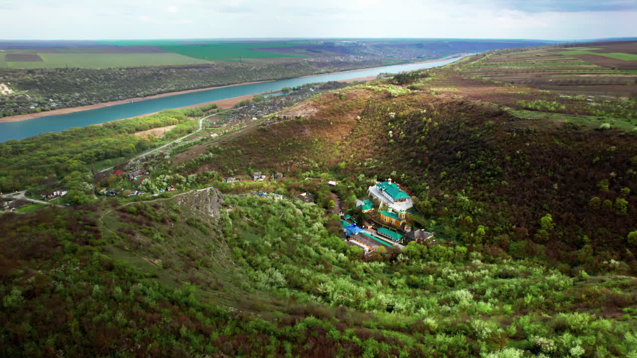 Aerial drone view of Saharna Monastery, Moldova. Monastery with churches located in a valley covered with lush forest. Dniester river on the background