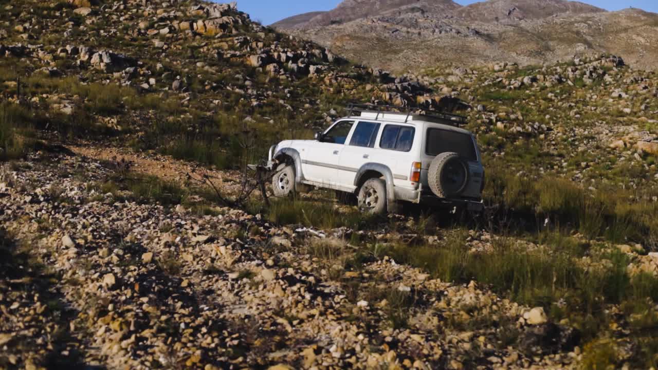 Slow motion tracking shot of SUV driving up rocky road between mountains