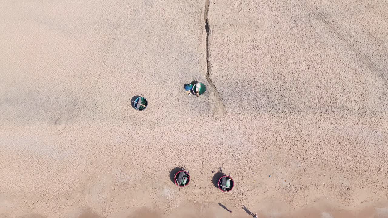 Drone rockets straight up from the white sand beach in Mui Ne, revealing rows of colorful swimming buckets parked on the shore against the turquoise sea and clear sky.