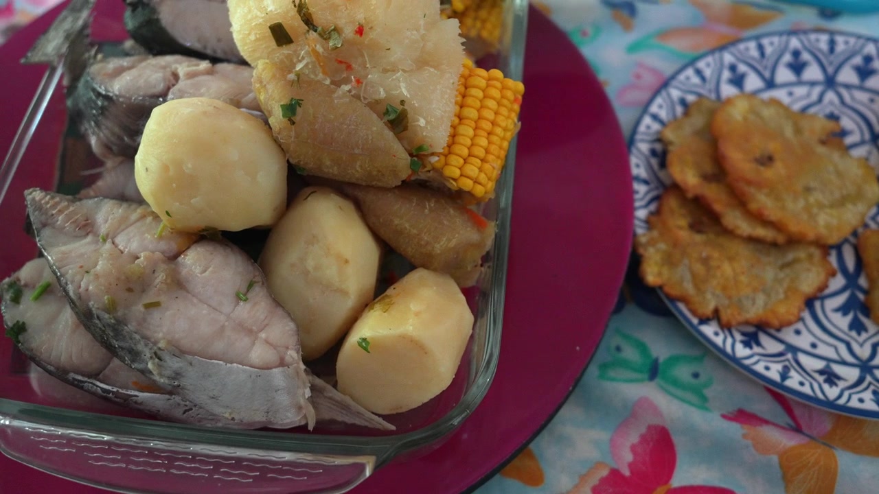 Primo piano di un vivace pasto di Santa Marta con sancocho di pesce e verdure a radice, con mais, yuca, patate e patacones, servito su piatti decorativi alla luce naturale del giorno