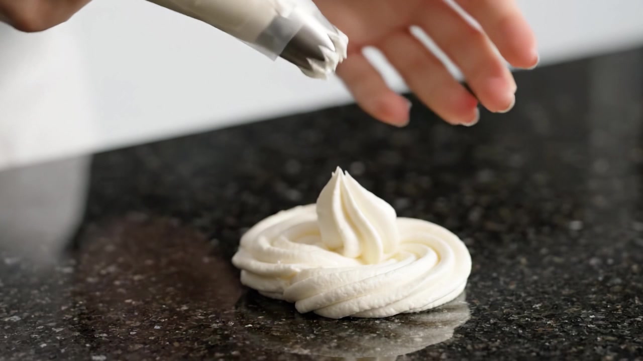 Uma Mão Habilidosa Aplicando Chantilly em uma Bancada Preta Elegante: A Arte da Decoração de Sobremesas Revelada Através de Redemoinhos Cremosos