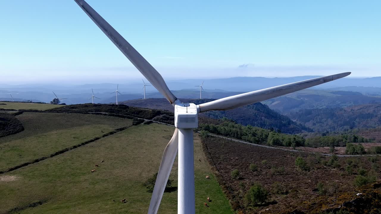volando por encima de la turbina eólica en el idílico entorno montañoso con pastoreo de ganado, cielo azul claro y soleado