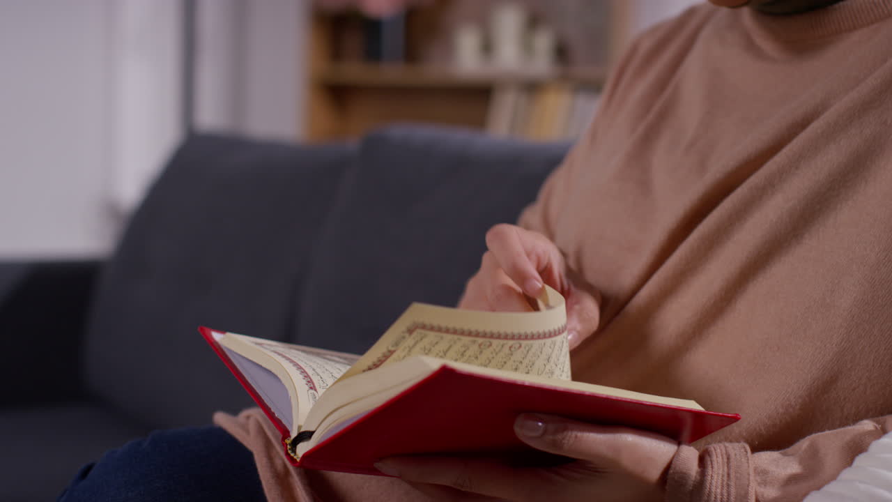 Close-up Wanita Muslim Duduk di Sofa di Rumah Membaca atau Mempelajari Al-Qur'an 5