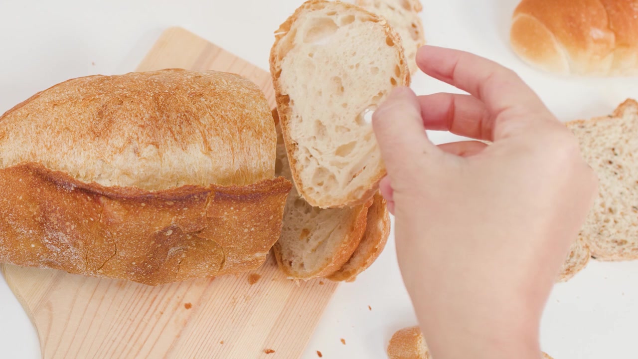 Overhead view of hands using a knife to slice crusty sourdough bread on white background.
